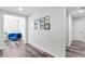 Bright hallway featuring wood-look floors, leading to a cozy sitting area with blue chair and decorative art at 8066 Bowery Dr, Winter Garden, FL 34787