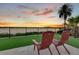 Patio chairs overlooking the water at sunset with artificial turf and travertine pavers at 17300 Pesce Loop, Montverde, FL 34756