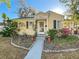 A quaint yellow home with vibrant landscaping, showcasing a welcoming walkway and charming architectural details under a sunny sky at 2107 University Dr, Orlando, FL 32804