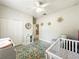Bedroom featuring a crib, glider, floral rug, and wall decor in neutral tones with a ceiling fan at 1913 Lazy Oaks Loop, St Cloud, FL 34771