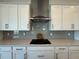 Close up of cooktop with stainless steel hood, white shaker cabinets, gray backsplash and quartz countertops at 2013 Divot Dr, Daytona Beach, FL 32124