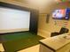 A modern golf simulator room setup with a projector screen, comfy seating, and golf clubs at 334 Prestwick Dr, Davenport, FL 33897