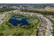 An aerial view of a community pond, surrounded by residential properties with an adjacent field, and treed landscape at 17394 Million Lakes Ct, Clermont, FL 34714