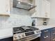 Close-up of modern kitchen featuring stainless steel stove, hood, marble backsplash, and white cabinets at 1739 Oak Blossom Dr, Davenport, FL 33837