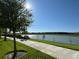 Scenic view of a lake with tree-lined shores and a paved path under a sunny sky at 5059 Lake Hamlin Trl, Winter Garden, FL 34787