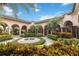 Clubhouse courtyard featuring a water fountain, palm trees, colorful landscaping, and a terracotta tile roof at 5512 Metrowest Blvd # 203, Orlando, FL 32811