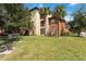 An exterior view of a condo surrounded by lush greenery and trees under a bright sky, with a lawn area at 5512 Metrowest Blvd # 203, Orlando, FL 32811