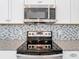 Close up of stainless steel oven and microwave with white cabinets and mosaic backsplash at 869 Taramundi Dr, Oviedo, FL 32765
