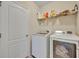 Functional laundry room with white washer and dryer, plus shelving for supplies at 5910 Windsong Oak Dr, Leesburg, FL 34748