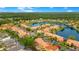 An aerial view captures colorful townhomes with red-tiled roofs lining a tranquil lake in a lushly landscaped neighborhood at 141 Pompano Beach Dr, Kissimmee, FL 34746