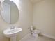 Well-lit half-bathroom with a pedestal sink, round mirror, and a toilet, designed for guests' convenience at 5074 Sparkling Water Way, Kissimmee, FL 34746