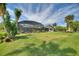 Expansive backyard featuring a large screened-in pool enclosure with a patio, lush greenery, and privacy landscaping at 29150 Beauclaire Dr, Tavares, FL 32778