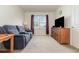 Inviting living room with cozy blue loveseat, carpeted floors, and a wooden TV console under the window at 9731 Pepper Tree Trl, Wildwood, FL 34785