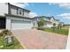 Attractive townhome showcasing a brick driveway, two-car garage, and neutral siding under a sunny, partly cloudy sky at 16450 Bird Of Paradise Ave, Clermont, FL 34714