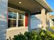 View of covered porch featuring a gray exterior, red shutters and door, and manicured landscaping at 5384 Palomino Pl, Apopka, FL 32712