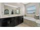 This bathroom features double sinks, dark wood cabinets, a large mirror, a soaking tub, and tiled floors at 885 Carmillion Ct, Groveland, FL 34736