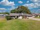 Charming single-story home with a lush green lawn, stone accents, and mature trees under a bright, cloudy sky at 9501 Holbrook Dr, Orlando, FL 32817