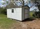 Exterior view of a small, white storage shed in a grassy yard under a large tree at 1328 Highland Cir, Kissimmee, FL 34744