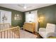Bedroom with a crib, dresser used as changing table, a cozy chair, and green walls at 7714 Lady Frances Way, Orlando, FL 32807