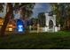 Nighttime view of an ornate gate and balustrade near a pond with a lighted fountain and gazebo in the background at 11450 Nellie Oaks Bnd, Clermont, FL 34711