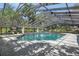 A stunning covered pool with ample patio space surrounded by lush trees and a glimpse of the blue sky at 11450 Nellie Oaks Bnd, Clermont, FL 34711