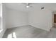 A minimalist bedroom with light gray floors, white walls, ceiling fan, and a glimpse into a bathroom at 239 S Lake Cortez Dr, Apopka, FL 32703