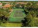 Aerial view of a green fenced-in tennis court surrounded by mature trees and bushes at 4730 Coral Castle Dr, Kissimmee, FL 34746