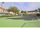 Green tennis court featuring a net and surrounded by green bushes and mature trees at 4730 Coral Castle Dr, Kissimmee, FL 34746