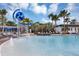 Bright community splashpad featuring an overhead water feature, lounge seating, fountains, palm trees, and a modern clubhouse at 8896 Reymont St, Orlando, FL 32827