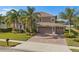 Charming two-story home featuring mature palm trees, a well-manicured lawn, and a three car garage on a brick driveway at 920 Nola Dr, Ocoee, FL 34761