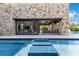 An outdoor living area featuring a stunning stone wall, a covered lounge, and a pool with tiled stepping stones at 1766 Alaqua Dr, Longwood, FL 32779