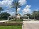 Community entrance with a guard house and palm trees under a cloudy blue sky at 1554 Corolla Ct, Reunion, FL 34747