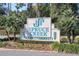 A Welcome sign to the Spruce Creek Fly-In Community with manicured landscaping and mature palm trees at 1845 Spruce Creek Blvd, Port Orange, FL 32128