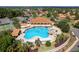 Aerial view of a community pool area with a rock grotto, clubhouse, and tennis courts at 5007 Belted Kingfisher Dr, Oxford, FL 34484