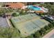 Aerial view of community tennis and pickleball courts near clubhouse and pool, with lush landscaping and parking area at 5007 Belted Kingfisher Dr, Oxford, FL 34484