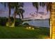 Manicured backyard view with lush green grass, palm trees, decorative landscape lighting, and a beautiful lake view at dusk at 8161 Via Rosa, Orlando, FL 32836
