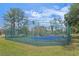 Outdoor tennis court surrounded by green fence and lush green grass, offering recreational opportunities at 8359 Grey Bark Ct, Sanford, FL 32771