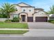 Inviting two-story home featuring a manicured lawn, palm trees, and a paver driveway leading to a two-car garage at 676 Bishop Bay Loop, Apopka, FL 32712