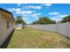 An umbrella stands on the concrete patio in the large backyard lined with a white fence under blue skies at 725 Laurel Way, Casselberry, FL 32707