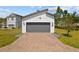 Front view of two car garage with gray door, brick paver driveway, and well manicured landscaping at 1873 White Feather Loop, Oakland, FL 34787