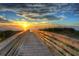 A wooden boardwalk leads to the beach with a stunning sunset over the horizon, and lush dunes at 2907 Sime St, New Smyrna Beach, FL 32168