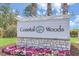 A welcoming sign for Coastal Woods is surrounded by colorful flowers, under a clear sky, and lush landscaping at 2907 Sime St, New Smyrna Beach, FL 32168