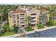 Aerial view of multi-story building featuring a complex with balconies, parking, palm trees, and manicured grounds at 7651 Whisper Way # 104, Reunion, FL 34747
