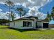 Side view of a modern single-story house with black shutters, a long driveway, and a lush green lawn at 6872 Sw 132Nd Pl, Ocala, FL 34473