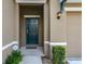 Inviting front entrance features a dark green door, decorative light fixture, and lush landscaping at 7618 Oakmoss Loop, Davenport, FL 33837