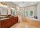 Bright, marble bathroom features dual sinks, granite countertops, glass enclosed shower, and soaking tub with arched windows at 12614 Hawkstone Dr, Windermere, FL 34786