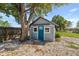 Exterior view of cozy shed conversion with blue door, surrounded by a lush lawn and mature trees at 1900 E Orange Ave, Eustis, FL 32726