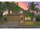 Inviting two-story home with a manicured lawn, mature trees, and warm exterior lighting at sunset at 108 Portstewart Dr, Orlando, FL 32828