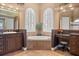 A bathroom showcasing dual vanities, a soaking tub, decorative mirrors, and two windows with plantation shutters at 10664 Emerald Chase Dr, Orlando, FL 32836