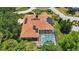 Aerial view of a backyard with a screened-in pool, tile roof, and solar panels amidst lush green trees at 128 Lake Region Cir, Winter Haven, FL 33881